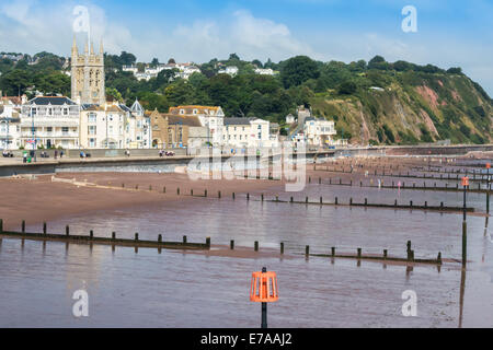 Die Strandpromenade in Teignmouth, Devon. Leisten erstrecken sich über den Strand ins Meer. Das Stadtzentrum und die Felsen im Hintergrund. Stockfoto