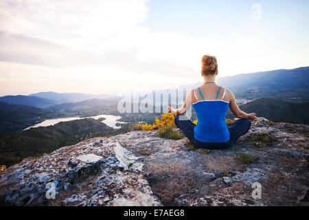 Junge Frau sitzt auf einem Felsen und Blick ins Tal genießen. Mädchen sitzt in Asana Position. Stockfoto