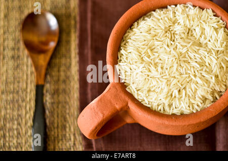 Tasse gefüllt mit rohem Reis und einem Holzlöffel auf einem Tisch Stockfoto