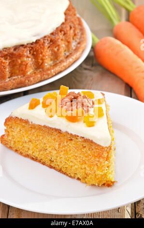 Stück Karotte-Kuchen mit Zuckerguss verziert, getrockneten Aprikosen und Walnuss auf weißen Teller auf rustikalen Tisch Stockfoto