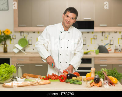 Frontansicht des kaukasischen Mann mit Koch Kleidung, Schneiden von Gemüse in der Küche, Lächeln Stockfoto