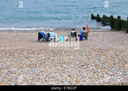 vier Leute sitzen auf steinigen Strand mit Blick auf das Meer. Stockfoto