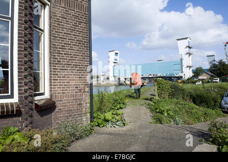 Rotterdam, Zuid-Holland, Niederlande, Holland. 10. September 2014. Ein Mann mäht den Rasen auf dem Deich und vor der niederländischen Ijjssel dam. Links ein kleiner Deich-Haus. Die Hollandse IJssel (holländische IJssel) verbindet Rotterdam mit der Nordsee. Im Hochwasserfall wäre das Wasser abfließen, weil die steigenden Meerwasser es aufhören würde. Der Fluss würde daher leicht seine Banken platzen. Es gab zwei Hauptgründe für die Suche nach einer Lösung für die Gefahr von Überschwemmungen: Erstens die Hollandse Issel durchfließt die niedrigsten liegenden Bereich der Niederlande. Zweitens ist dies eine der m Stockfoto