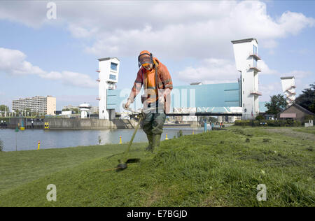 10. September 2014 - ist ein Mann auf dem Deich und vor der holländischen Ijssel Staumauer Rasenmähen. Die Hollandse IJssel (holländische IJssel) verbindet Rotterdam mit der Nordsee. Im Hochwasserfall wäre das Wasser abfließen, weil die steigenden Meerwasser es aufhören würde. Der Fluss würde daher leicht seine Banken platzen. Es gab zwei Hauptgründe für die Suche nach einer Lösung für die Gefahr von Überschwemmungen: Erstens die Hollandse Issel durchfließt die niedrigsten liegenden Bereich der Niederlande. Zweitens ist dies eines der bevölkerungsreichsten Gebiete der Niederlande. Zunächst, dam ich Bau ein halb geschlossen Stockfoto