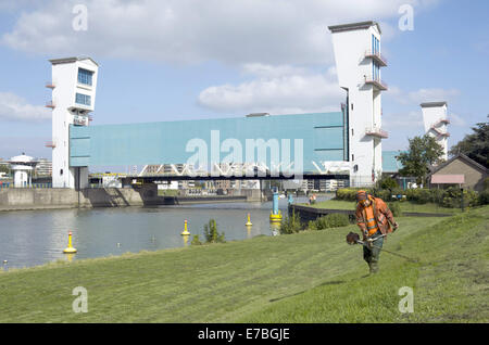 Rotterdam, Zuid-Holland, Niederlande, Holland. 10. September 2014. Ein Mann mäht den Rasen auf dem Deich und vor der holländischen Ijssel-Staumauer. Die Hollandse IJssel (holländische IJssel) verbindet Rotterdam mit der Nordsee. Im Hochwasserfall wäre das Wasser abfließen, weil die steigenden Meerwasser es aufhören würde. Der Fluss würde daher leicht seine Banken platzen. Es gab zwei Hauptgründe für die Suche nach einer Lösung für die Gefahr von Überschwemmungen: Erstens die Hollandse Issel durchfließt die niedrigsten liegenden Bereich der Niederlande. Zweitens ist dies eines der bevölkerungsreichsten Gebiete der N Stockfoto