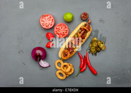 Moderne Hot Dog mit Lamm Wurst, Tomaten, Zwiebelringe, Jalapeno, rote Paprika, mexikanische Salsa auf Beton Tisch