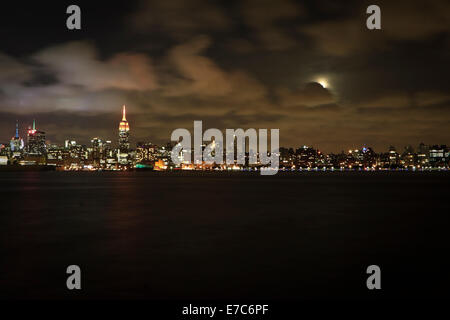 Empire State Building in der Nacht mit einem Vollmond spähen hinter Wolken. Stockfoto