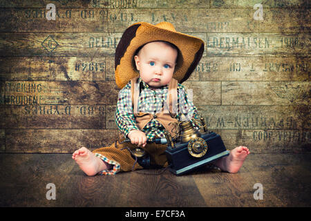 Süßes Kind in Cowboy-Hut mit Retro-Telefon auf Hintergrund der Bretter Stockfoto