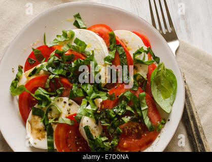 Caprese-Salat mit Tomaten, Basilikum, Mozzarella-Käse auf weißen Teller mit Gabel auf Seite Stockfoto