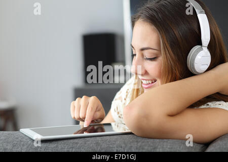Glückliche Frau hören der Musik von einem Tablet sitzt auf einer Couch zu Hause Stockfoto
