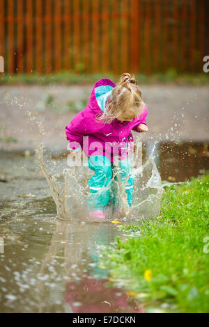 Glückliches kleine Mädchen spielt in einer Pfütze Stockfoto