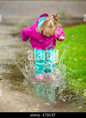 Glückliches kleine Mädchen spielt in einer Pfütze Stockfoto