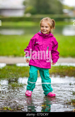 Glückliches kleine Mädchen spielt in einer Pfütze Stockfoto