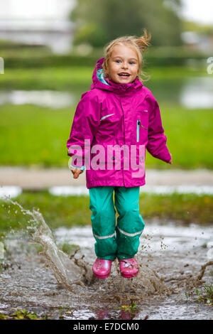 Glückliches kleine Mädchen spielt in einer Pfütze Stockfoto