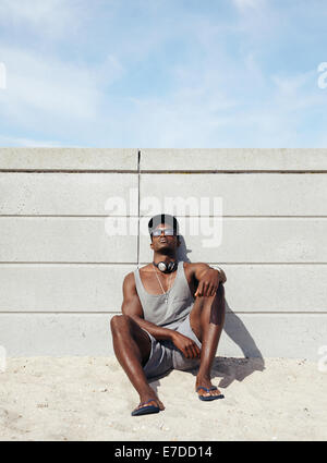 Muskulösen jungen Mann entspannen am Strand. Afrikanischer Mann lehnt sich an eine Wand sitzen. Stockfoto