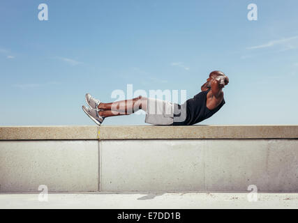 Athlet Sit gegen Himmel. Afrikanische Männermodel Bewegung in der Natur mit Textfreiraum. Stockfoto