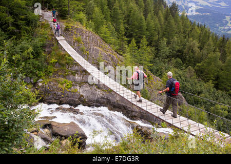 Wanderer auf der Tour Du Mont Blanc überqueren eine Hängebrücke über den Fluss Schmelzwasser aus den Gletscher von Bionnassay; Stockfoto