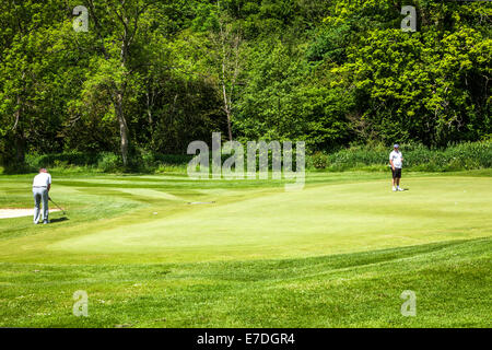 Zwei Golfer spielen auf ein Putting-Green in der Nähe ein Loch auf einem typischen englischen Golfplatz. Stockfoto