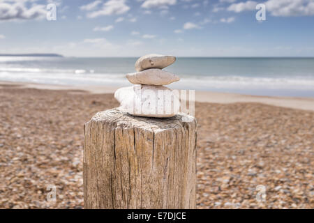 Cairn oder Steinhaufen balancieren auf einem hölzernen Buhne Post mit der Schindel Strand, Meer und blauer Himmel im Hintergrund Stockfoto