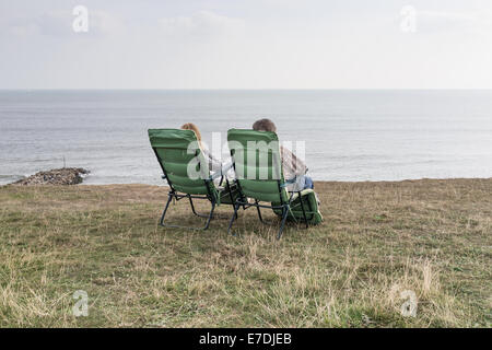 Zwei ältere Menschen sitzen auf Stühlen auf einer Klippe mit Blick auf das Meer Stockfoto