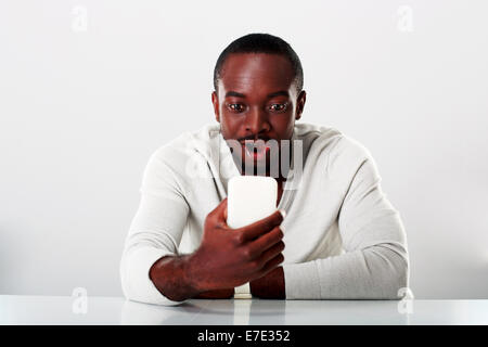 Überrascht afrikanischen Mann sitzt auf dem Tisch und Blick auf smartphone Stockfoto