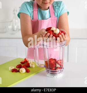 Mädchen legen Erdbeeren und Bananen in einen Mixer, 8 Jahre Stockfoto