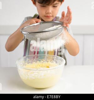 Junge Sichtung Mehl in eine Schüssel mit Kuchenteig, 7 Jahre Stockfoto