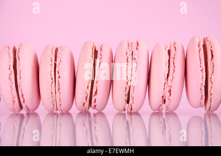 Reihe von rosa Macarons auf reflektierende Oberfläche vor einem rosa Hintergrund. Stockfoto