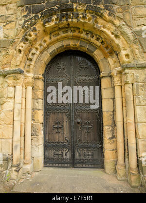 Dunkle braune Holztür mit riesigen reich verzierte eiserne Scharniere umgeben von dekorativen steinernen Torbogen in der historischen Kirche in Bakewell, England Stockfoto