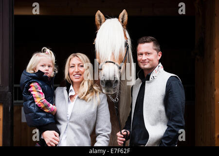 Junge Familie stehend mit einem Tyrolean Haflinger vor einem Stall, Nord-Tirol, Österreich Stockfoto