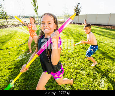 Kaukasische Kinder spielen im Sprinkler im Hinterhof Stockfoto