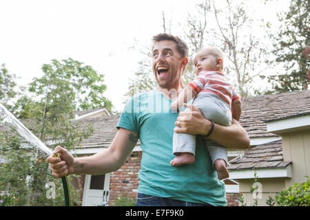 Kaukasische Vater hält Baby und Bewässerung von Pflanzen Stockfoto