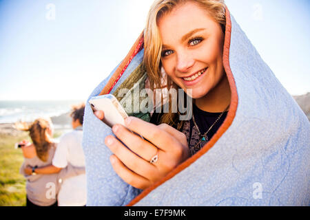 Frau mit Handy in Decke auf ländlichen Hügel Stockfoto