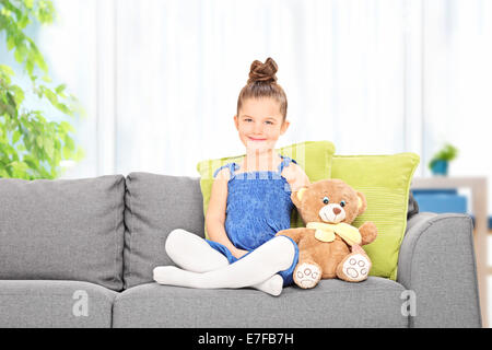 Niedliche kleine Mädchen mit Teddy-Bär auf dem Sofa zu Hause sitzen Stockfoto