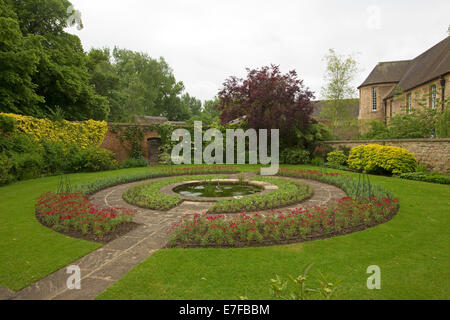 Formale ummauerten Garten mit Weg über smaragdgrünen Rasen führt, Wassereigenschaft, umgeben von großen kreisförmigen Gartenbeete mit roten Blumen runden Stockfoto