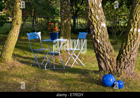 Blauer Tisch, Stühle & Dekoration im Garten mit Bäumen, Stockfoto