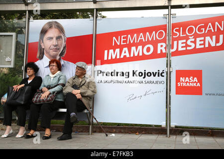 (140916)--SARAJEVO, 16. September 2014 (Xinhua)--Leute sitzen neben ein Poster eines Kandidaten für den Wahlkampf in Sarajevo, Bosnien und Herzegowina, 16. September 2014. Kampagne der allgemeinen Wahlen in Bosnien und Herzegowina weiterhin bis zum 12. Oktober, dem Tag für die Wahl. (Xinhua/Haris Memija) (Dzl) Stockfoto