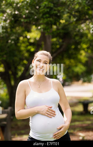 Porträt von glücklichen schwangeren Bauch zu berühren und in die Kamera Lächeln im Stadtpark stehen Stockfoto