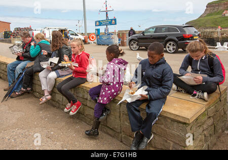 Gruppe von Kindern, schwarz und weiß, Essen von Fisch und Chips emporter Shop unter englischen Küste Stadt Whitby Stockfoto