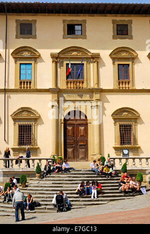 Arezzo, Toskana, Italien. Piazza Grande (Stadt Hauptplatz) Palazzo della Fraternita dei Laici. Menschen sitzen auf Stufen Stockfoto