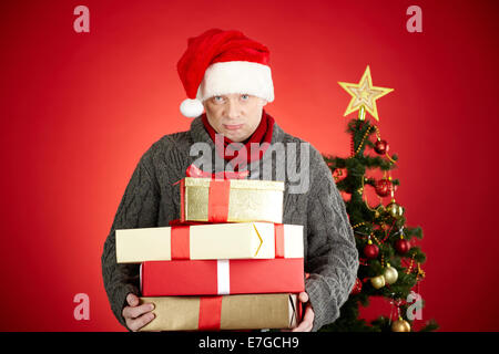 Trauriger Mann in Santa Cap holding Stack von Geschenken und Blick in die Kamera Stockfoto