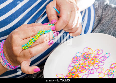 Frauen mit bunten Nägeln machen einen Webstuhl Kautschukarmband mit einem Haken. Hände in der Nähe. Junge Mode-Neukonzeption. Stockfoto