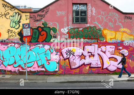 Frau mit Handy zu Fuß vor der Wand Graffiti, Dublin, Republik Irland, Europa. Stockfoto