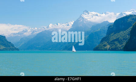 Herrliches Panorama der Berge mit schneebedeckten Gipfeln. Auf die Oberfläche des Sees Segelboot segeln. Wolkenloser blauer Himmel Stockfoto