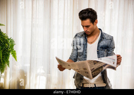 Hübscher junger Mann zu Hause lesen Zeitung, stehend Stockfoto