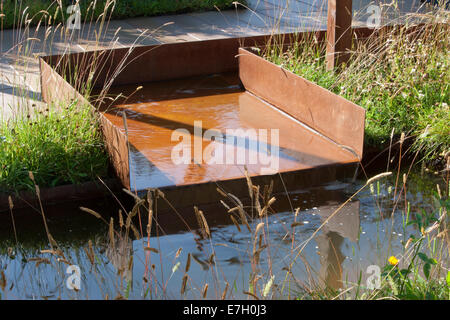 Wildtierfreundlicher Garten mit Rillenwasser aus rostem Kornstahl in einem kleinen Teich und Pflanzen von Ziergräsern in Großbritannien Stockfoto