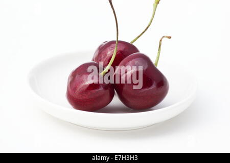 Drei frische Kirschen in einer weißen Schale auf weißem Hintergrund Stockfoto