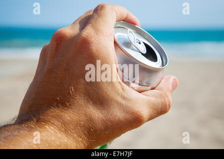 Aluminium kann Bier in eine männliche Hand mit Strand und Meer im Hintergrund Stockfoto