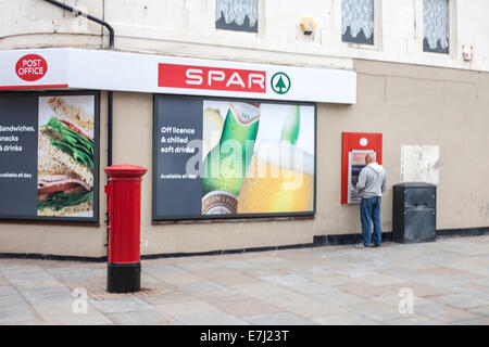 Ein Mann an einem Geldautomaten ATM bei Spar-Supermarkt und Postamt in Amble Northumberland UK Stockfoto