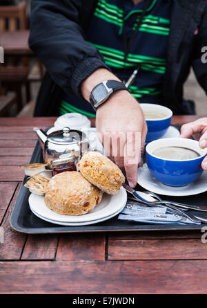 Tatton Park Cheshire England. Mans Hände nehmen Tasse Kaffee aus Fach gefüllt mit Gebäck, Marmelade, Butter, Teekanne, Zucker, Löffel. Stockfoto